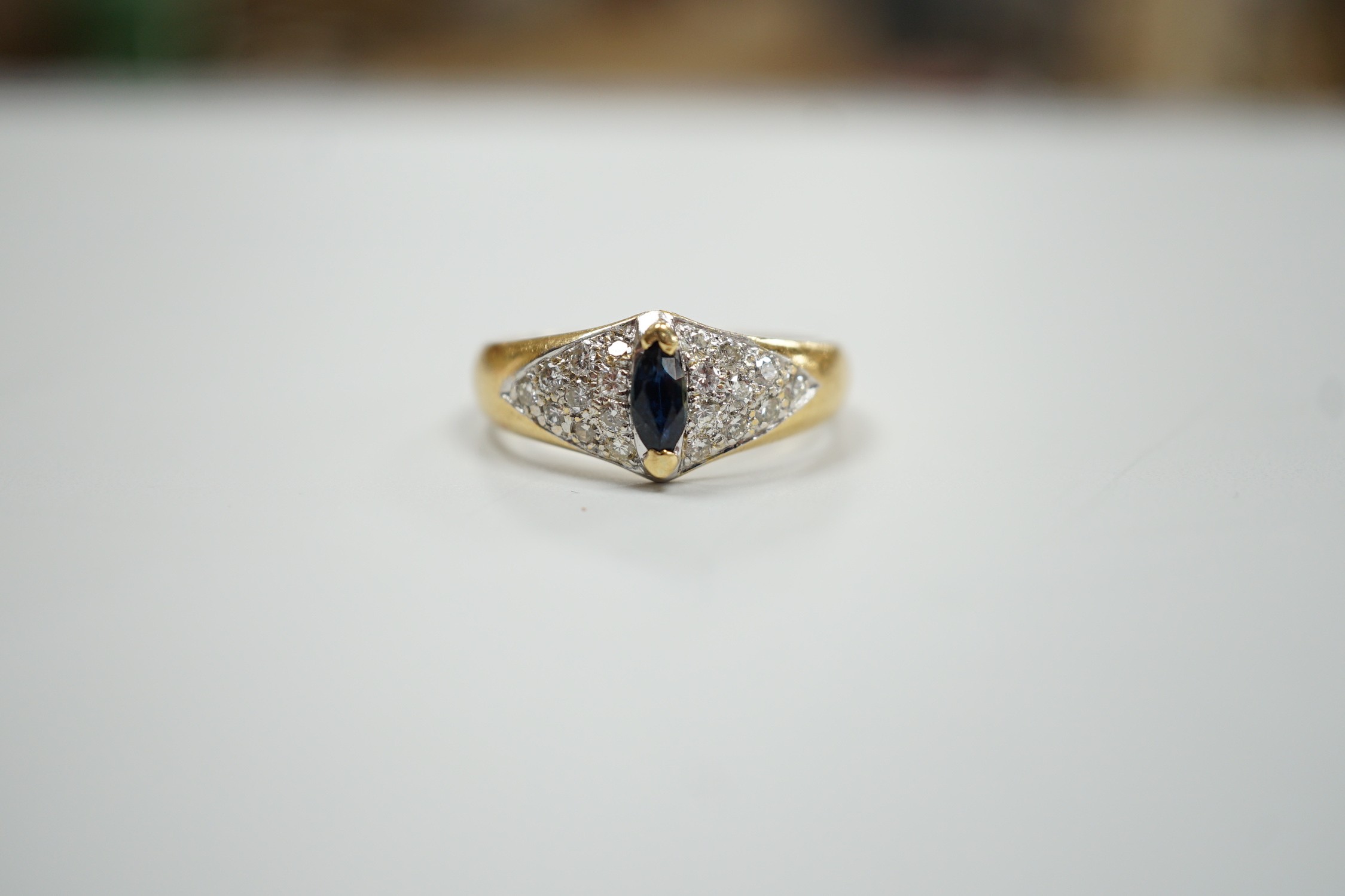 A modern 18ct gold and single stone marquise cut sapphire set dress ring, with pave set diamond shoulders, size R, gross weight 5 grams.